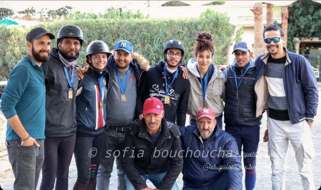 Onze cavaliers, grooms et membres d’équipe photographiés ensemble après une compétition, plusieurs portant une médaille sur ruban bleu. Amine Regaieg se tient au milieu du rang du fond.